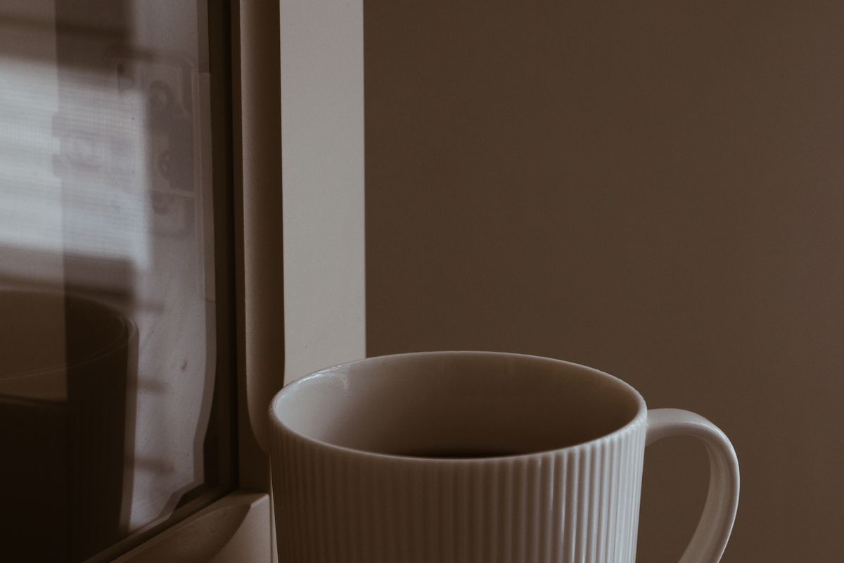 A pale ceramic mug of coffee on a windowsill in soft morning light