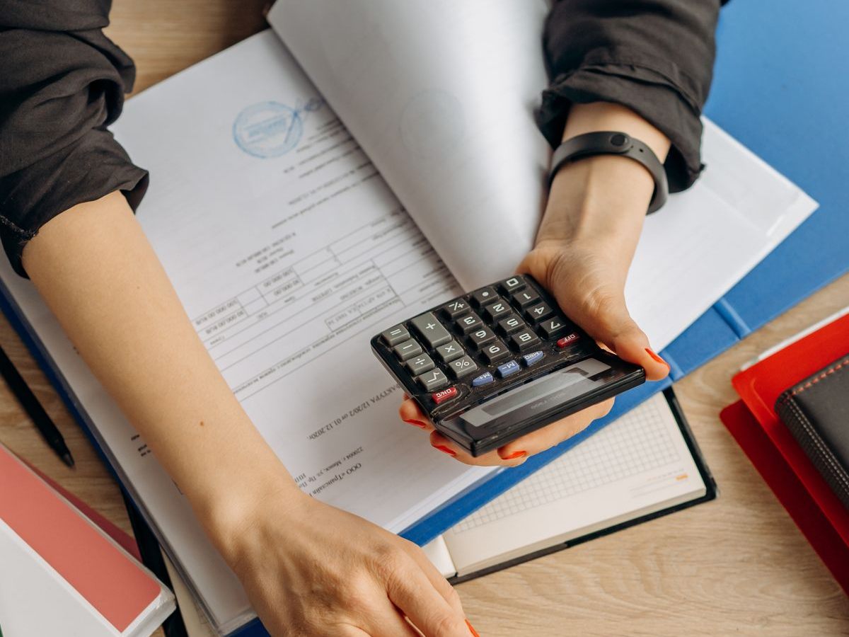 An accountant working through documents with a calculator beside a laptop