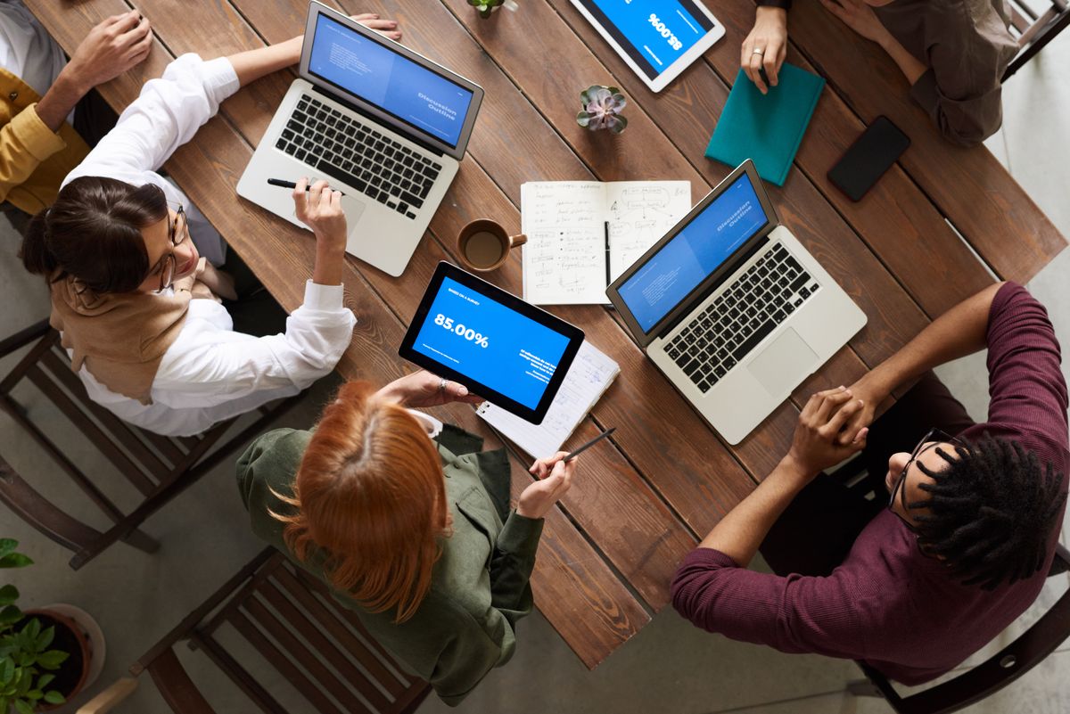 An agency team working around a wooden table with laptops and tablets
