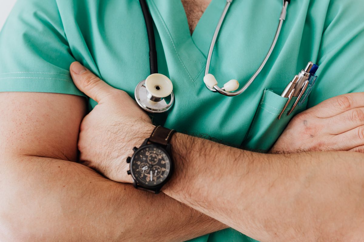 A clinician in scrubs with a stethoscope and arms folded