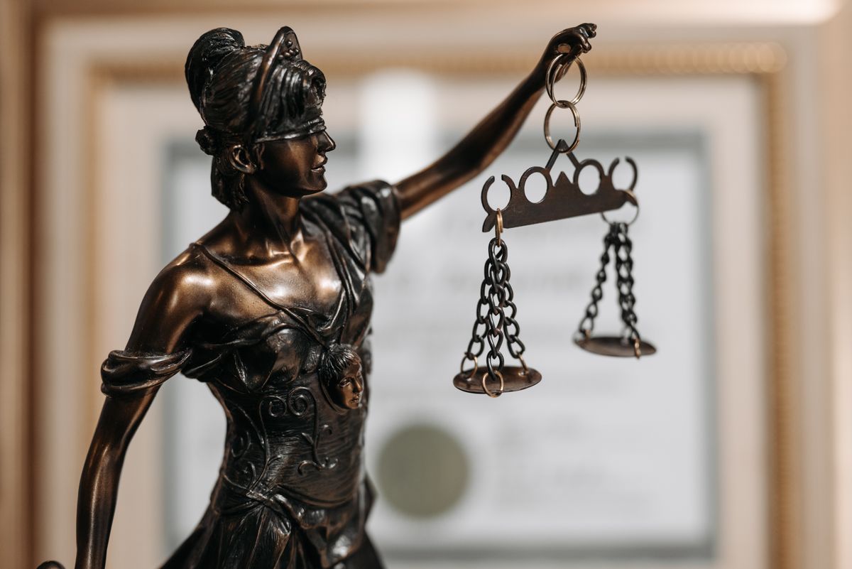 A statue of Lady Justice holding scales in front of a framed certificate