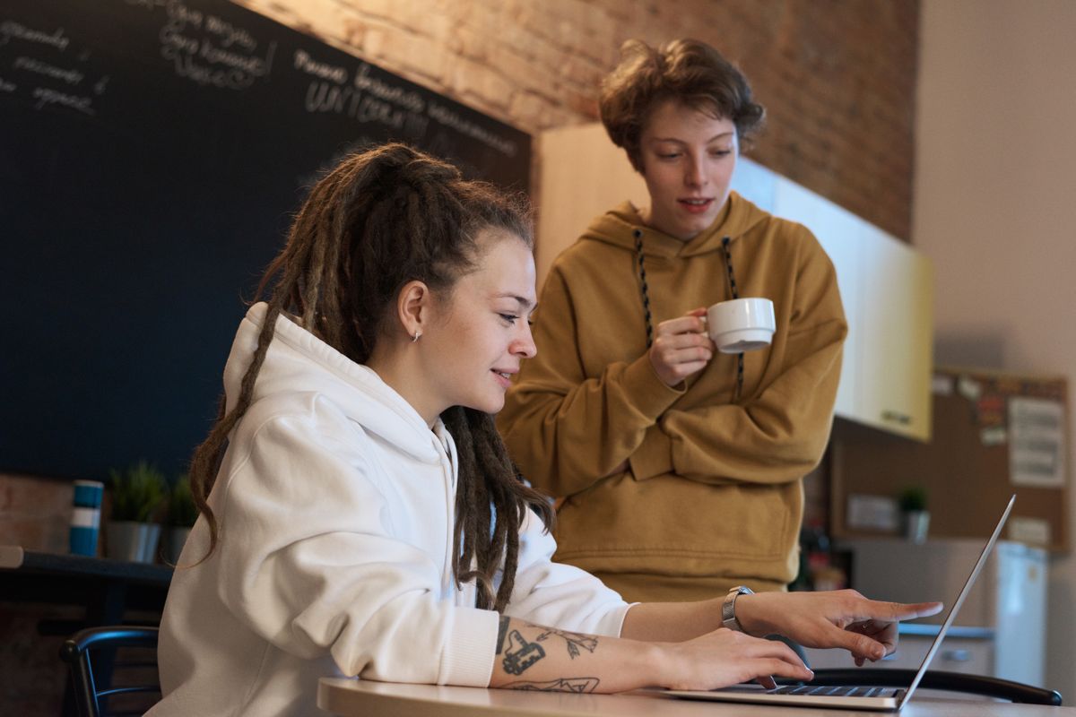 Two colleagues at a desk, one showing the other something on a laptop