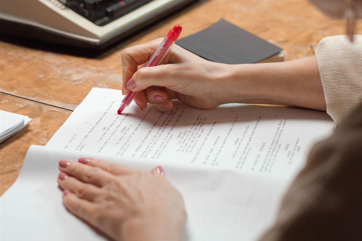 A person edits a typed page with a red pen beside a typewriter