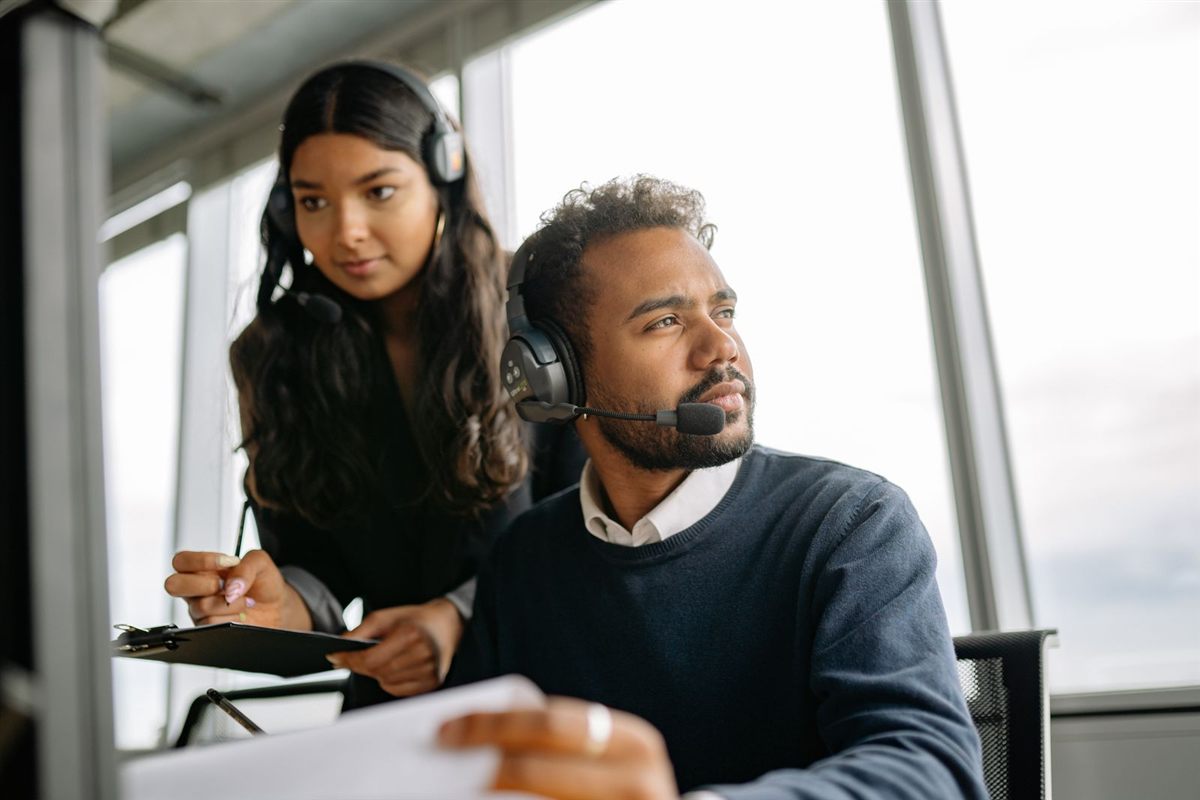 Two support agents with headsets work together at a bright office desk